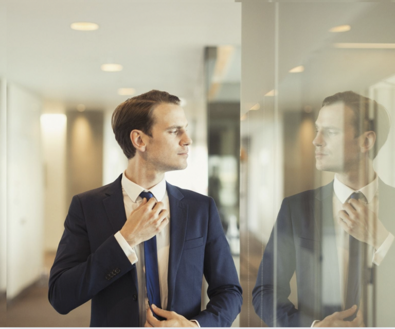 a person in a suit adjusting their tie in front of a mirror
